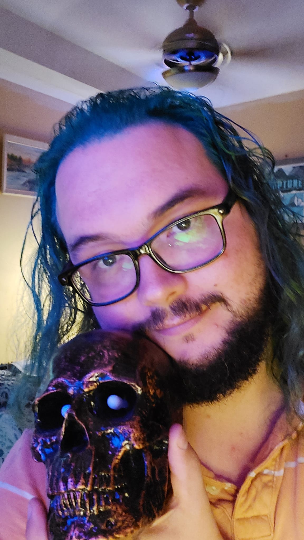 A man with long green hair sits in a computer chair holding a plastic skull, photo 1